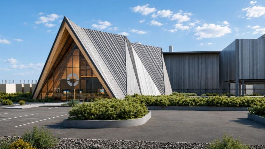A modern architectural complex with a prominent A-frame structure clad in metal panels and large glass windows, adjacent to a long, low building also covered in vertical metal siding.